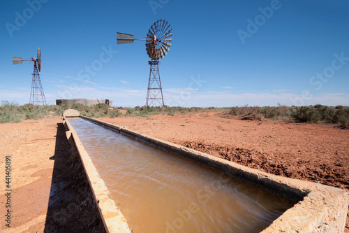 Looking along a full water trough with windmills and tanks in the background