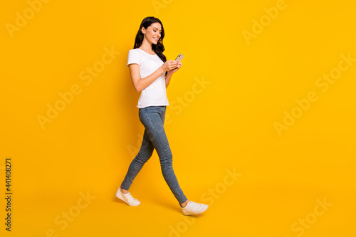 Full length profile side photo of pretty girl go empty space hold smartphone red message isolated on yellow color background