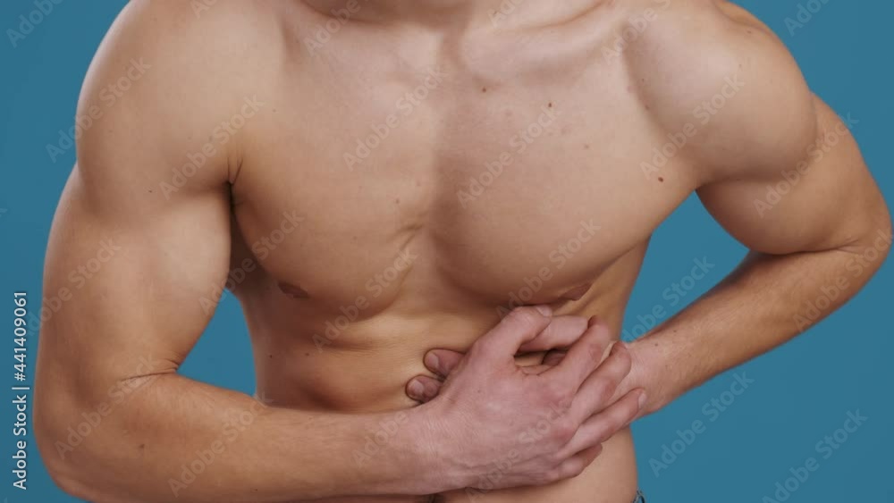 Stomach pain. Unrecognizable shirtless man suffering from pain in left side, touching his painful belly, blue background Stomach pain. Unrecognizable shirtless man suffering from pain in left side, touching his painful belly, blue background