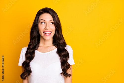 Photo of cute cunning young woman wear white t-shirt showing tongue looking empty space isolated yellow color background