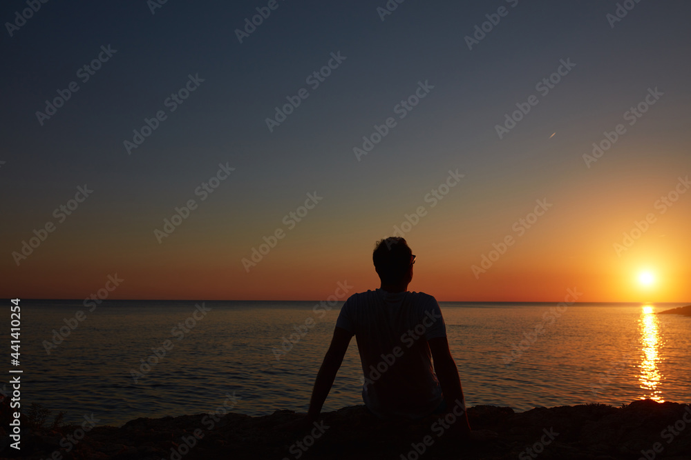 Silhouette of a man watching sunset over distant horizon.