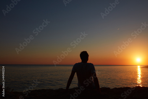 Silhouette of a man watching sunset over distant horizon. © astrosystem