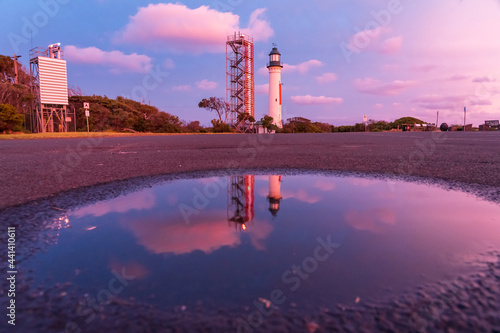 A lighthouse and signal tower at sunset reflected in a puddle photo