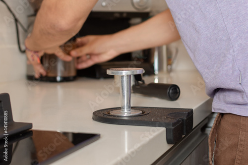 Close-up and focus on the coffee tamper while a man's hands take the ground coffee in the background