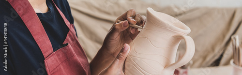 Φωτογραφία partial view of young african american woman sculpting clay pot with stick in po