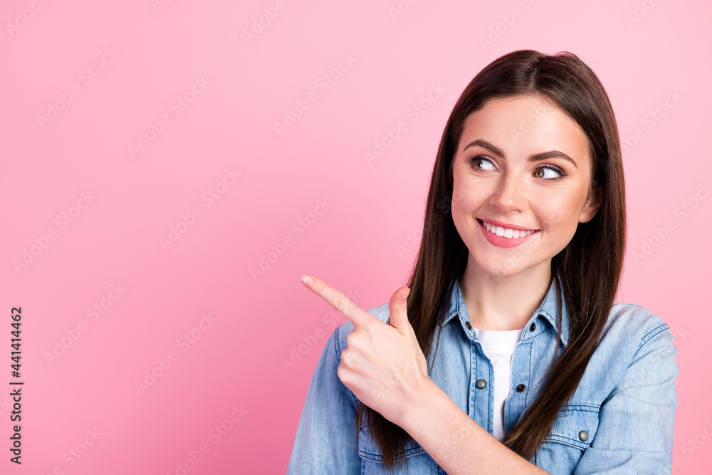 Photo of nice positive happy young woman look point finger empty space smile isolated on pastel pink color background Photo of nice positive happy young woman look point finger empty space smile isolated on pastel pink color background