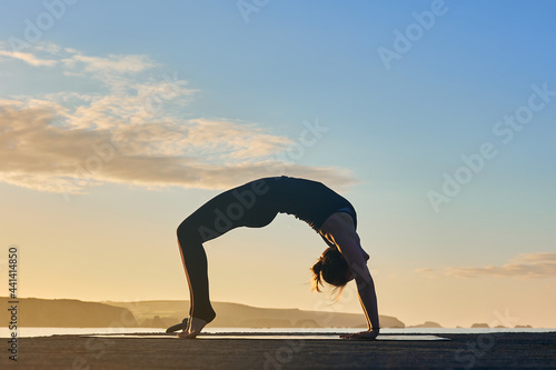 wheel or inverted arch. yoga posture outdoors, in silhouette of a Hispanic woman.