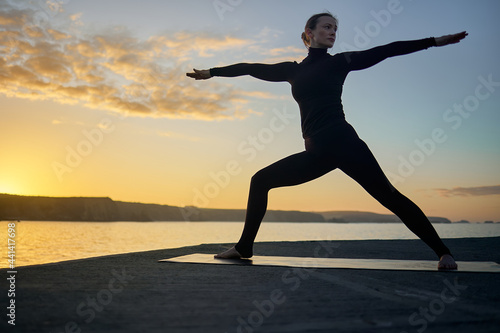 yoga pose of the warrior at sunset outdoors in silhouette of woman