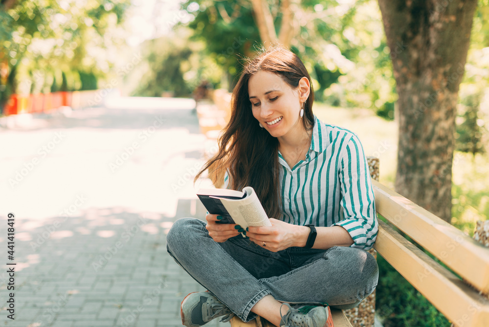 Photo of young woman reading and enjoying a book on the bench in public park. Photo of young woman reading and enjoying a book on the bench in public park.