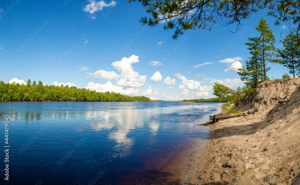 The sandy pure beach of the forest river in Karelia in northern Russia. Pine branch on top of the photo. White clouds are reflected in calm water as in a mirror. The sandy pure beach of the forest river in Karelia in northern Russia. Pine branch on top of the photo. White clouds are reflected in calm water as in a mirror.