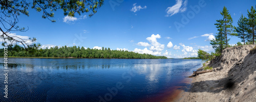 Panoramic view to the picturesque landscape of the white beach and the blue surface of the water in the frame of pine branches. Wonderful calm sunny summer day.