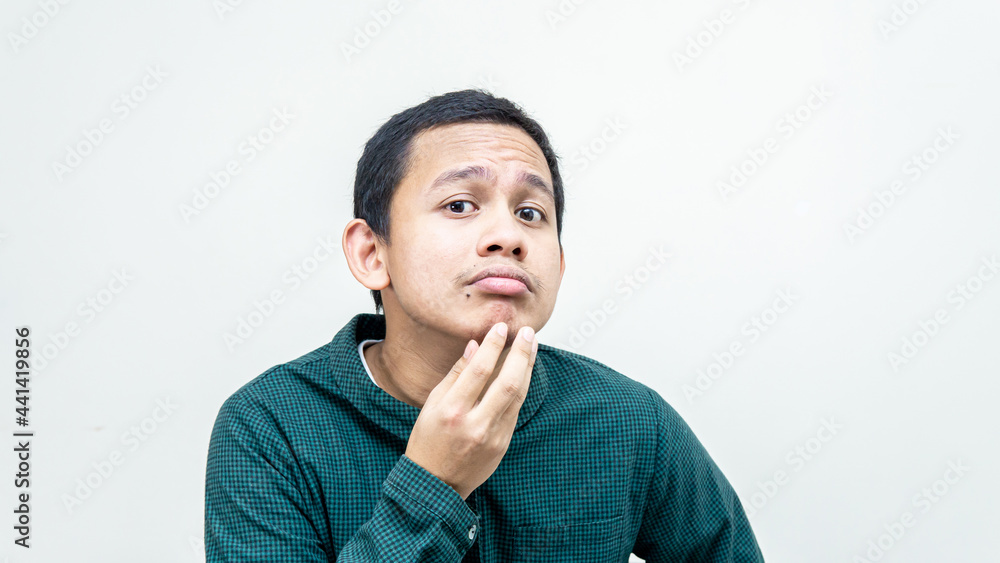 A portrait of young Asian Malay man holding chin checking his face for skin care and beauty concepts, studio shot isolated white background with copy space. A portrait of young Asian Malay man holding chin checking his face for skin care and beauty concepts, studio shot isolated white background with copy space.