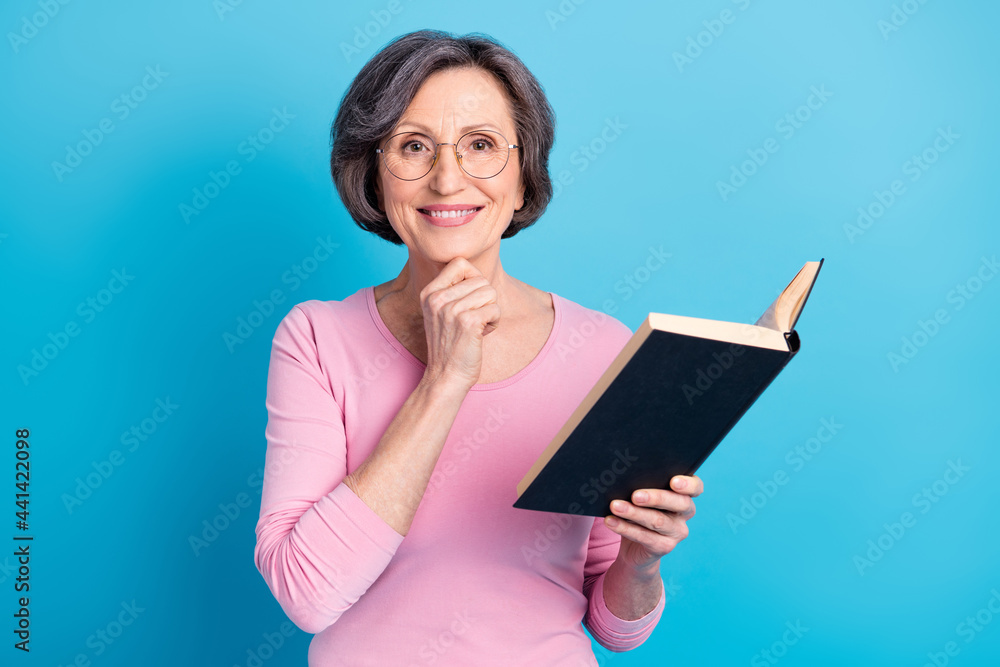 Photo of happy beautiful charming sweet woman in glasses thinking reading book isolated on blue color background Photo of happy beautiful charming sweet woman in glasses thinking reading book isolated on blue color background