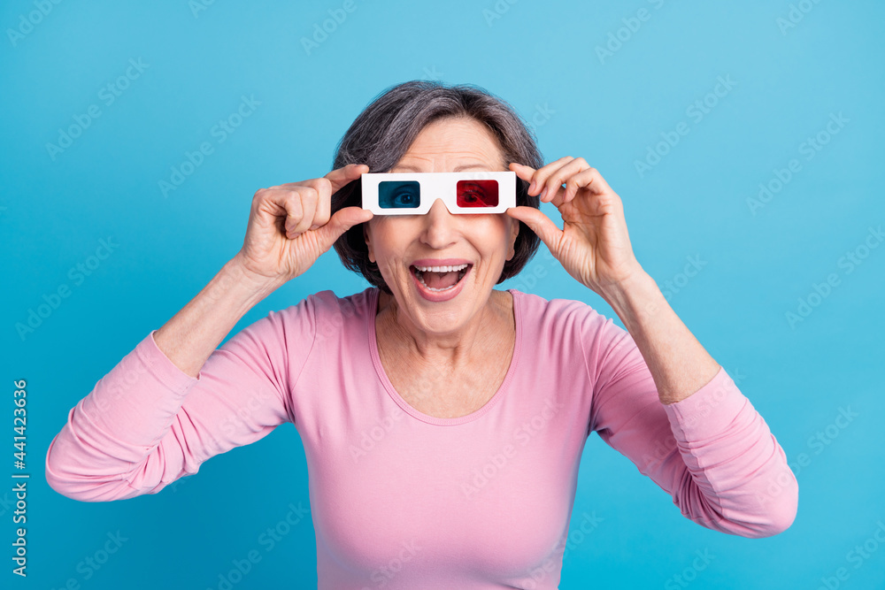 Photo of happy excited crazy cheerful smiling mature woman watching movie in 3d glasses isolated on blue color background Photo of happy excited crazy cheerful smiling mature woman watching movie in 3d glasses isolated on blue color background
