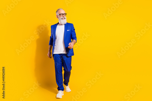 Full length body size view of attractive chic cheerful man walking isolated over bright yellow color background photo