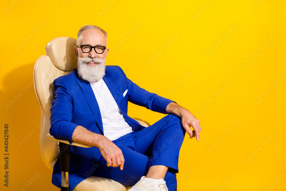 Portrait of attractive elegant imposing cheerful man sitting in office chair director isolated over bright yellow color background Portrait of attractive elegant imposing cheerful man sitting in office chair director isolated over bright yellow color background