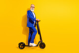 Full length body size profile side view of elegant funky man riding eco kick scooter isolated over bright yellow color background