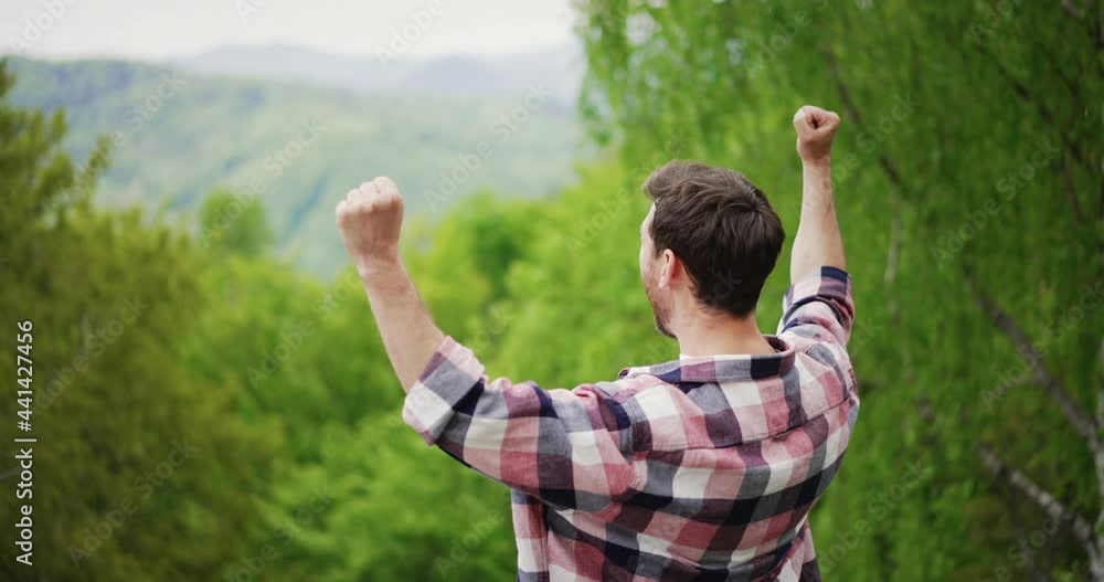 Close up of man traveller standing on top of mountain hill and rejoices his success and achievement by screaming and raising hands up in the air. Close up of man traveller standing on top of mountain hill and rejoices his success and achievement by screaming and raising hands up in the air.