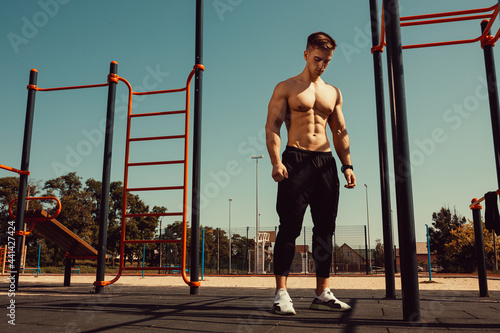 guy with a beautiful athletic body posing while standing next to the horizontal bars