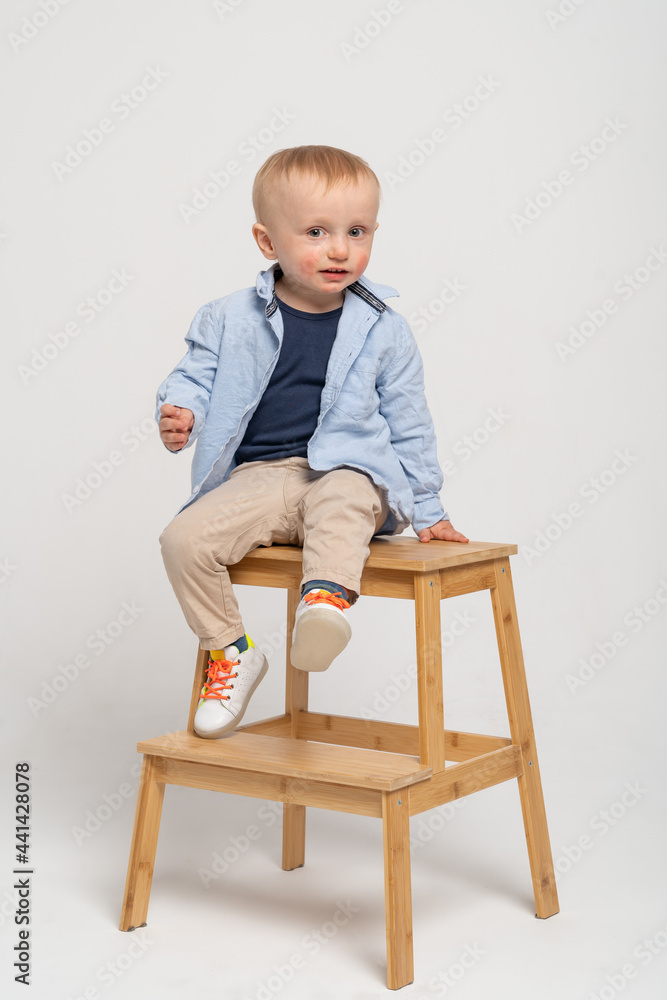 Little boy on the white background making funny face - blonde caucasian child sitting on the wooden ladder Little boy on the white background making funny face - blonde caucasian child sitting on the wooden ladder