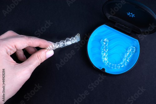 Woman holding invisible transparent aligners or plastic orthodontic braces. Black package with a box, clear-plastic retainers