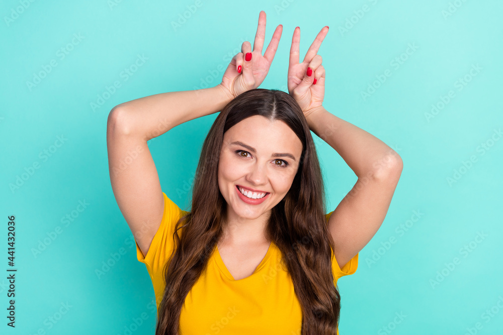 Photo of adorable childish young lady wear yellow outfit smiling showing two v-signs head isolated turquoise color background