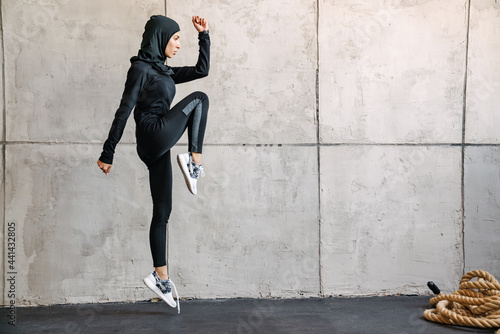 Young muslim woman in hijab jumping while working out indoors