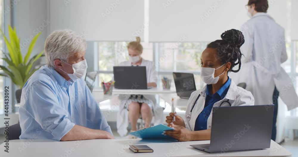 Female doctor and patient in protective masks talking in clinic Female doctor and patient in protective masks talking in clinic