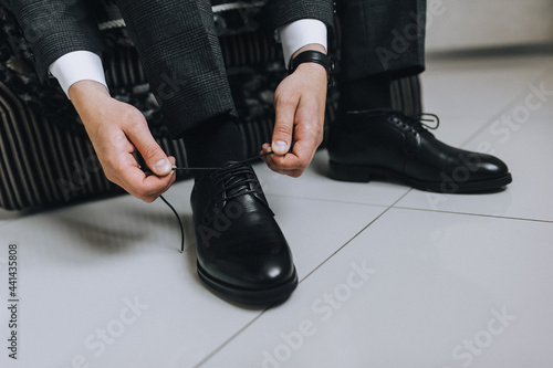 A man, a businessman, a groom ties long shoelaces on black leather shoes, shiny with cream, with his hands in a jacket close-up. Photography, concept.
