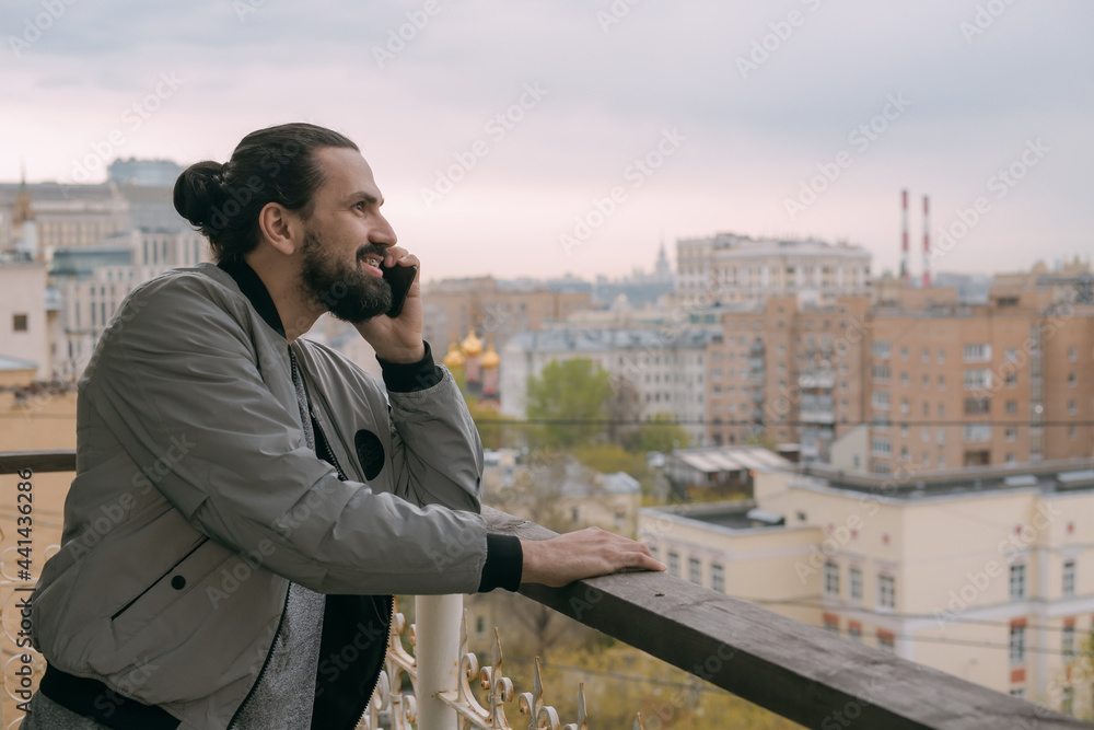 Portrait of a young handsome man with a phone on the balcony overlooking the city.
