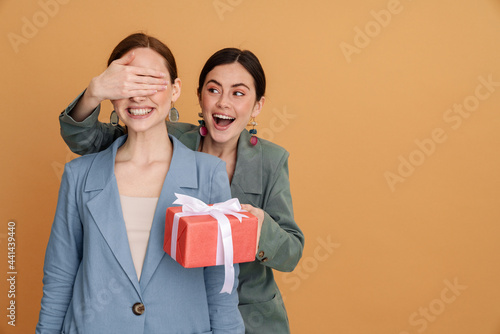 Young woman covering her friend's eyes while giving present