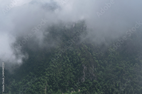 Forest and mountains in fog in cloudy weather. Beautiful landscape of National Park of Russia top view from drone. Dark thundercloud envelops green coniferous forest and sharp peaks of mountains.