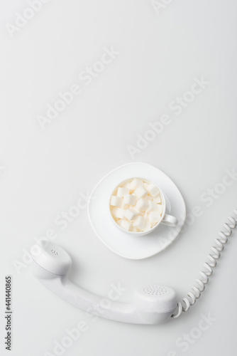 top view of sugar cubes in cup with saucer near retro phone on white