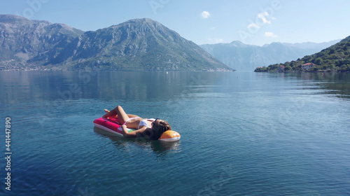 AERIAL. Young women enjoy floating on a mattress at the sea. Mountains on background.