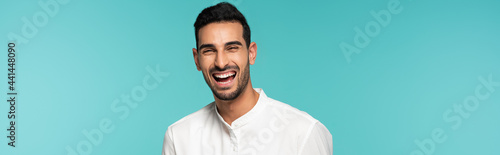 Happy arabian man looking at camera isolated on blue, banner