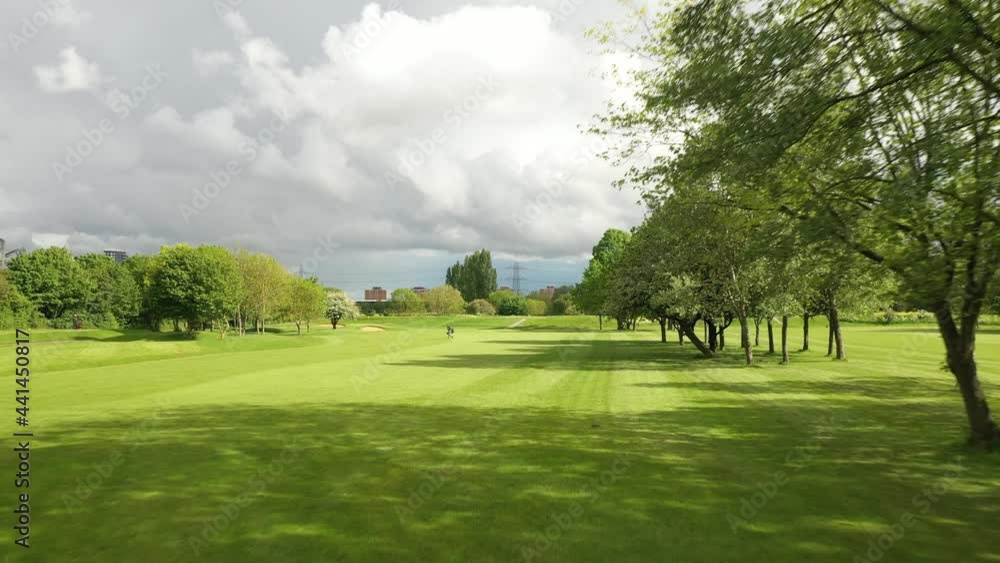 Male player carrying bag with golf clubs and walking across fairway. Overcast sky