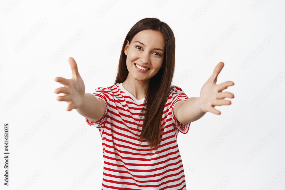 Portrait of beautiful 20s girl reaching for hug, spread hands sideways and smiling, embracing friend, wanting to hold smth in her arms, standing against white background Portrait of beautiful 20s girl reaching for hug, spread hands sideways and smiling, embracing friend, wanting to hold smth in her arms, standing against white background