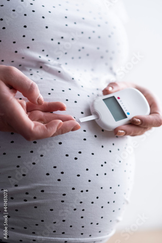 A pregnant woman holds a blood sugar meter in her hand and brings a test strip to a drop of blood on her finger photo