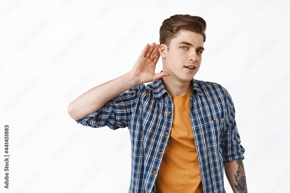Intrigued young guy eavesdropping, boy overhear gossips, hold hand near ear and trying to hear conversation, standing over white background Intrigued young guy eavesdropping, boy overhear gossips, hold hand near ear and trying to hear conversation, standing over white background