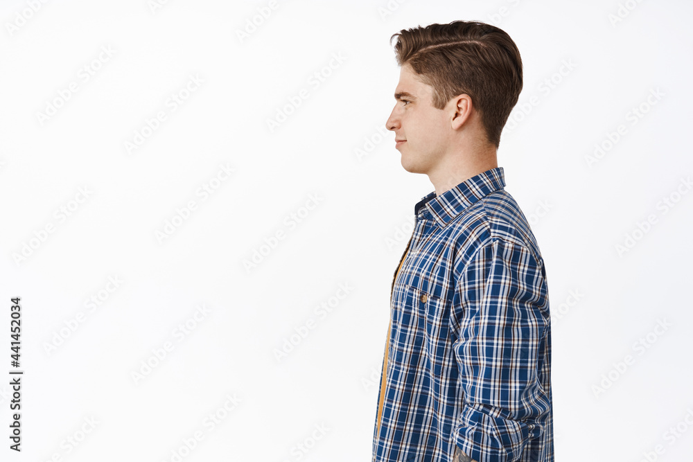 Profile portrait of young caucasian guy, boy with hairstyle and clean side of face, smiling and looking aside at empty space left, standing against white background Profile portrait of young caucasian guy, boy with hairstyle and clean side of face, smiling and looking aside at empty space left, standing against white background