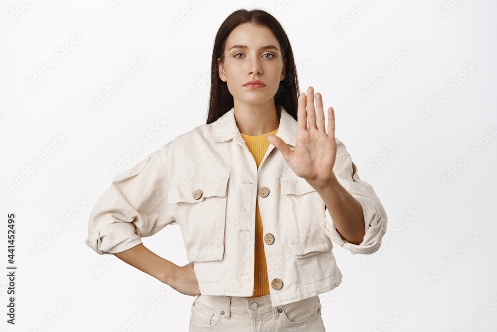 Enough, keep distance. Serious girl extend hand in taboo, stop sign, say no to smth bad, prohibit or restrict smth, rejecting offer, standing over white background Enough, keep distance. Serious girl extend hand in taboo, stop sign, say no to smth bad, prohibit or restrict smth, rejecting offer, standing over white background