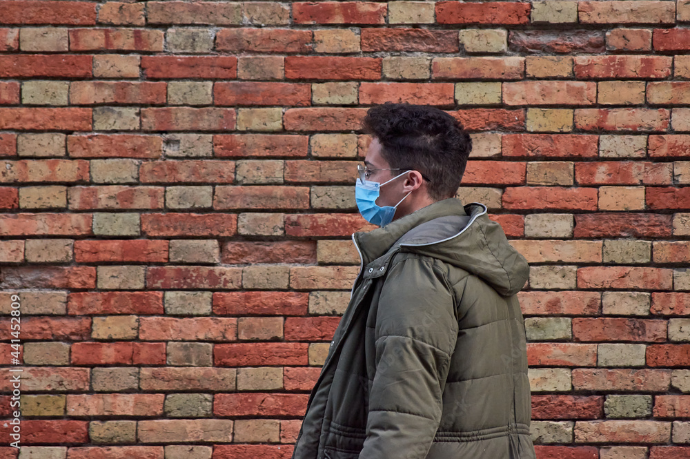 A portrait of a young Hispanic male in a medical mask against a brick wall A portrait of a young Hispanic male in a medical mask against a brick wall