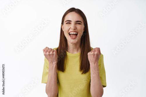 Yeah winner. Successful and lucky woman winning, triumphing, shouting for joy from win, celebrating victory, standing joyful against white background photo