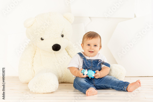 a small child six months old in blue jeans plays at home near a large Teddy bear