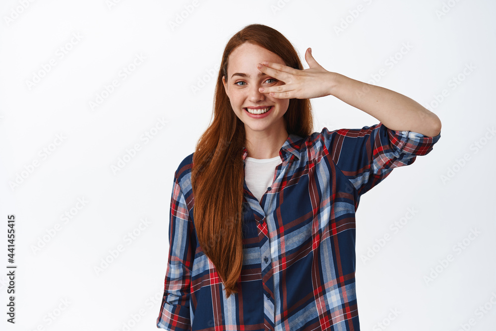 Beautiful redhead woman with white smile, open eyes, peeking through fingers and looking happy, showing natural ginger hair and clean skin, studio background Beautiful redhead woman with white smile, open eyes, peeking through fingers and looking happy, showing natural ginger hair and clean skin, studio background