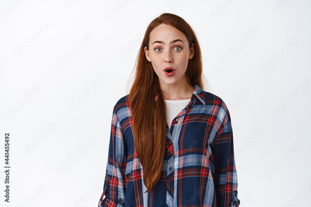Wow super cool. Impressed teen redhead girl, gasp and stare astoished at camera, looking with excitement at awesome promo in store, standing over white background Wow super cool. Impressed teen redhead girl, gasp and stare astoished at camera, looking with excitement at awesome promo in store, standing over white background