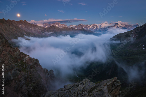 Mountain peaks emerging from the fog at the blue hour while the moon rises, Stelvio National Park, Ponte di Legno, Lombardy, Italy