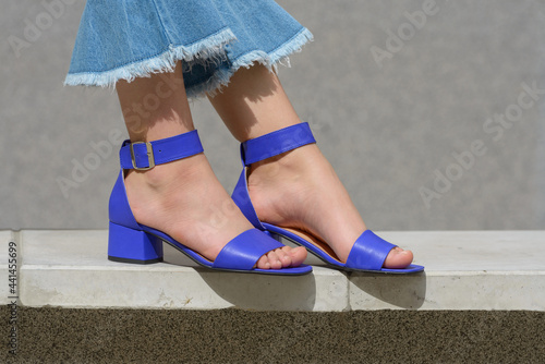 Women's legs in blue denim jeans and sandals in the city street. Trendy elegant casual outfit. Details of everyday summer look. photo