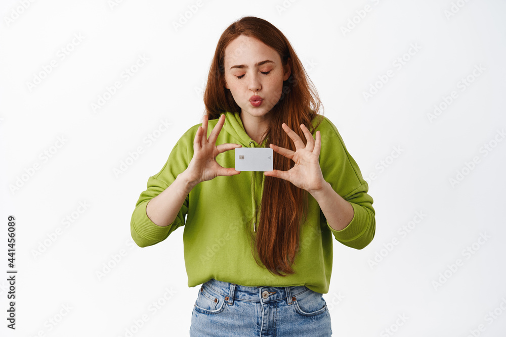 Girl likes shopping, kissing her credit card with closed eyes, buying something, paying for purchase, making online order, white background Girl likes shopping, kissing her credit card with closed eyes, buying something, paying for purchase, making online order, white background