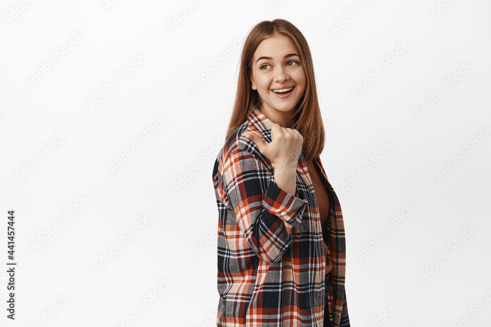 This way. Portrait of blond young woman smiling, pointing and looking left behind her shoulder, showing way, advertisement or copy space for your promotion text, white background